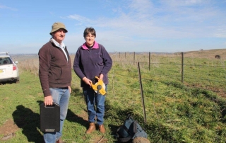 Man and woman by fence in farmland.