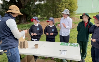 A woman is showing students how to plant a tree.