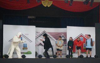 Two performers dressed as cats and four primary-school aged children perform on-stage.