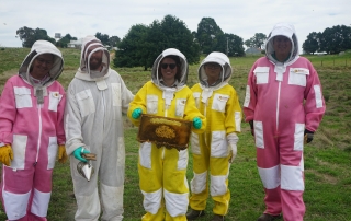 Five people wearing protective clothing hold a frame of honey from a bee hive.